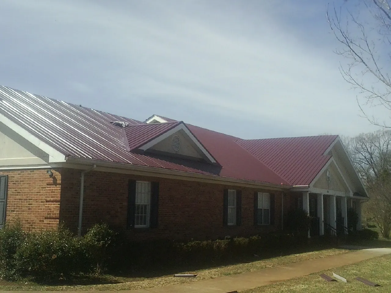 Red metal roof with gabled entries on a long brick building, from a Hail Damage Roof Repair job in Fort Hill