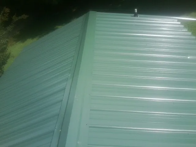 New green metal panels meeting at the ridge of a roof — Flat Roof Repair work by our crew in Fort Hill