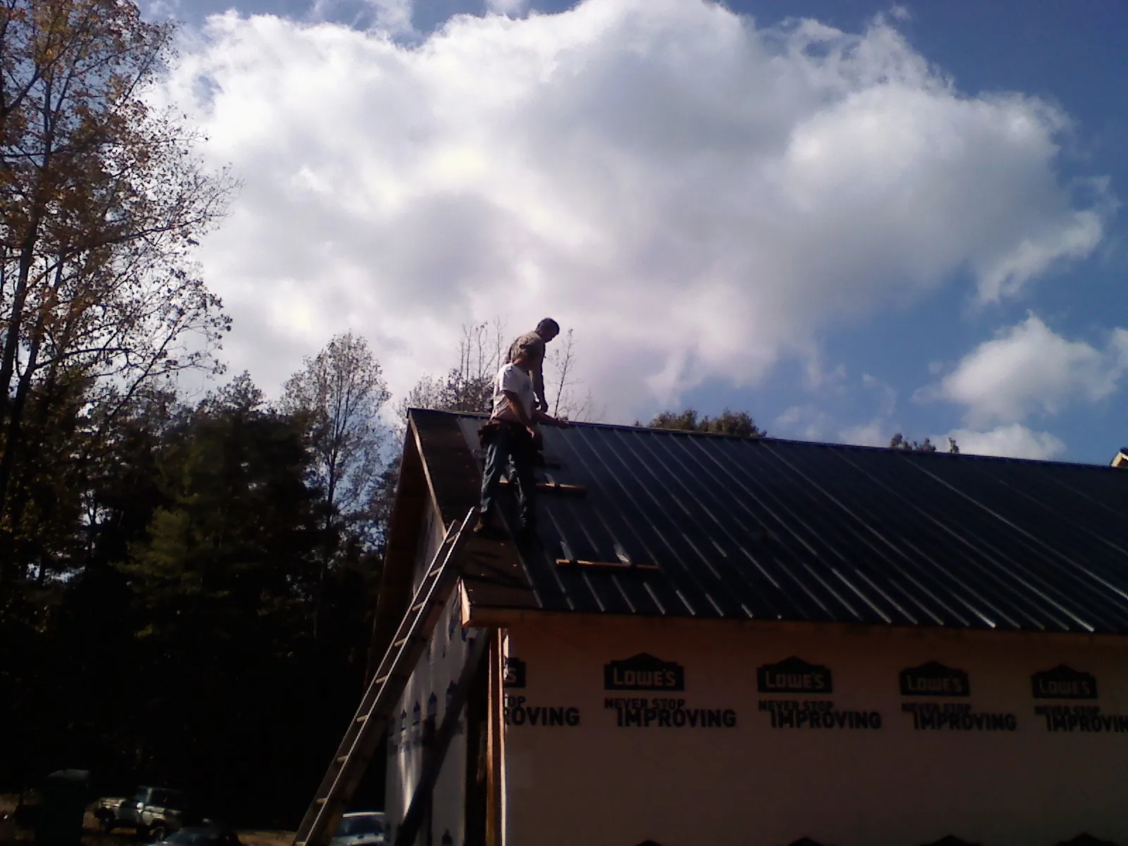 Roofer fastening dark metal panels high against a cloudy sky, from a Roof Inspection job in Fort Hill