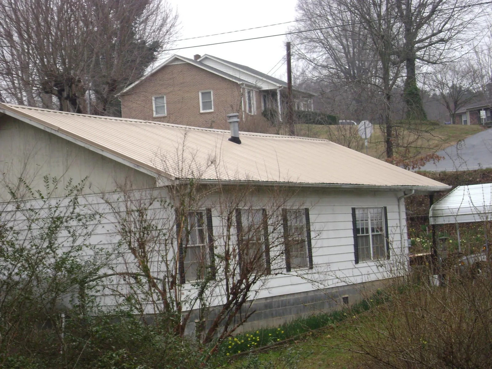 Tan metal roof on a white sided house set into a hillside — Commercial Roofing by Roofing Brothers in Fort Hill
